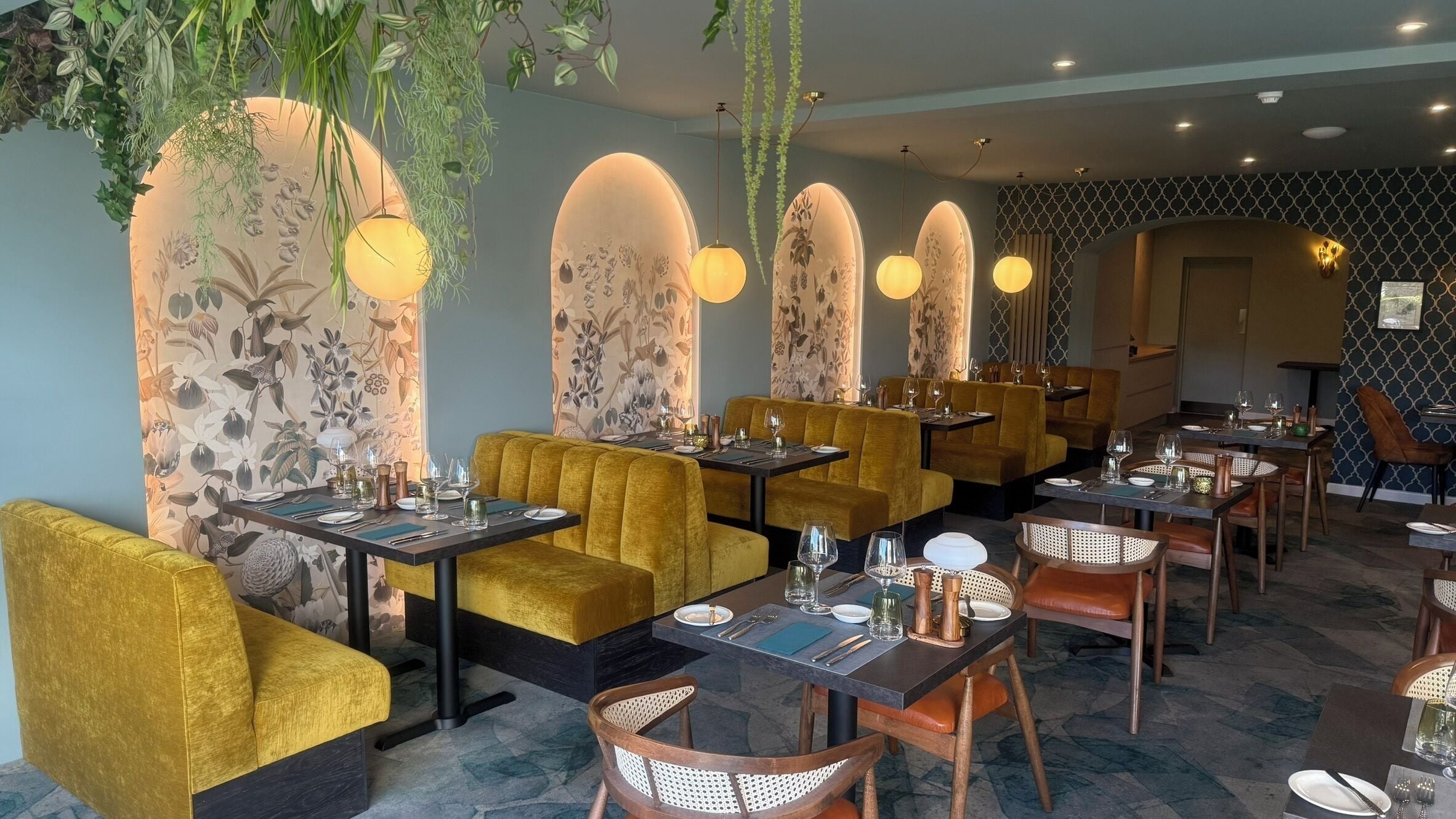 A restaurant interior with seating arrangements, tables set for dining, and hanging plants.