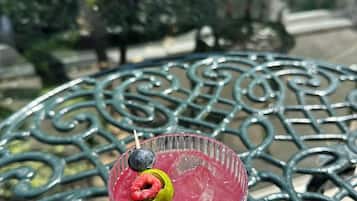 Un verre contenant une boisson rouge, décoré d’une framboise et de myrtilles, posé sur une table en métal à l’extérieur.
