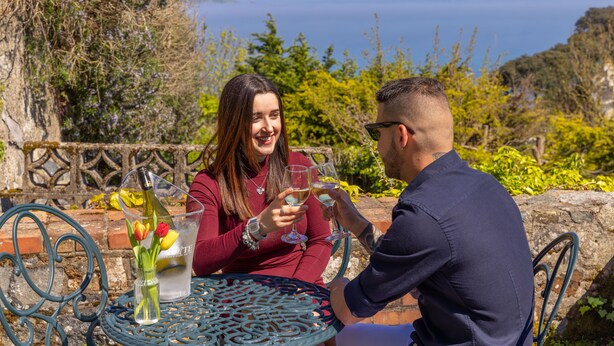 A couple sitting at a table with a view of the sea, holding wine glasses. - The Pandora Hotel (St. Peter Port)