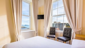 A hotel room with two large windows, a bed, two chairs, and a TV on the wall. - The Pandora Hotel (St. Peter Port)