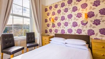 A hotel room with a large bed, two chairs, a nightstand, and a window with curtains.