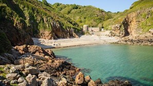 A coastal landscape with rocky terrain, a clear turquoise sea, and a small building on the shore. - The Pandora Hotel (St. Peter Port)