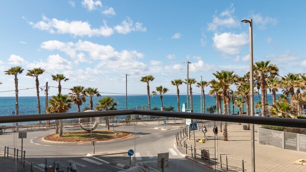 Eine Küstenstraße mit Palmen, einer Kreisverkehr und Blick aufs Meer.