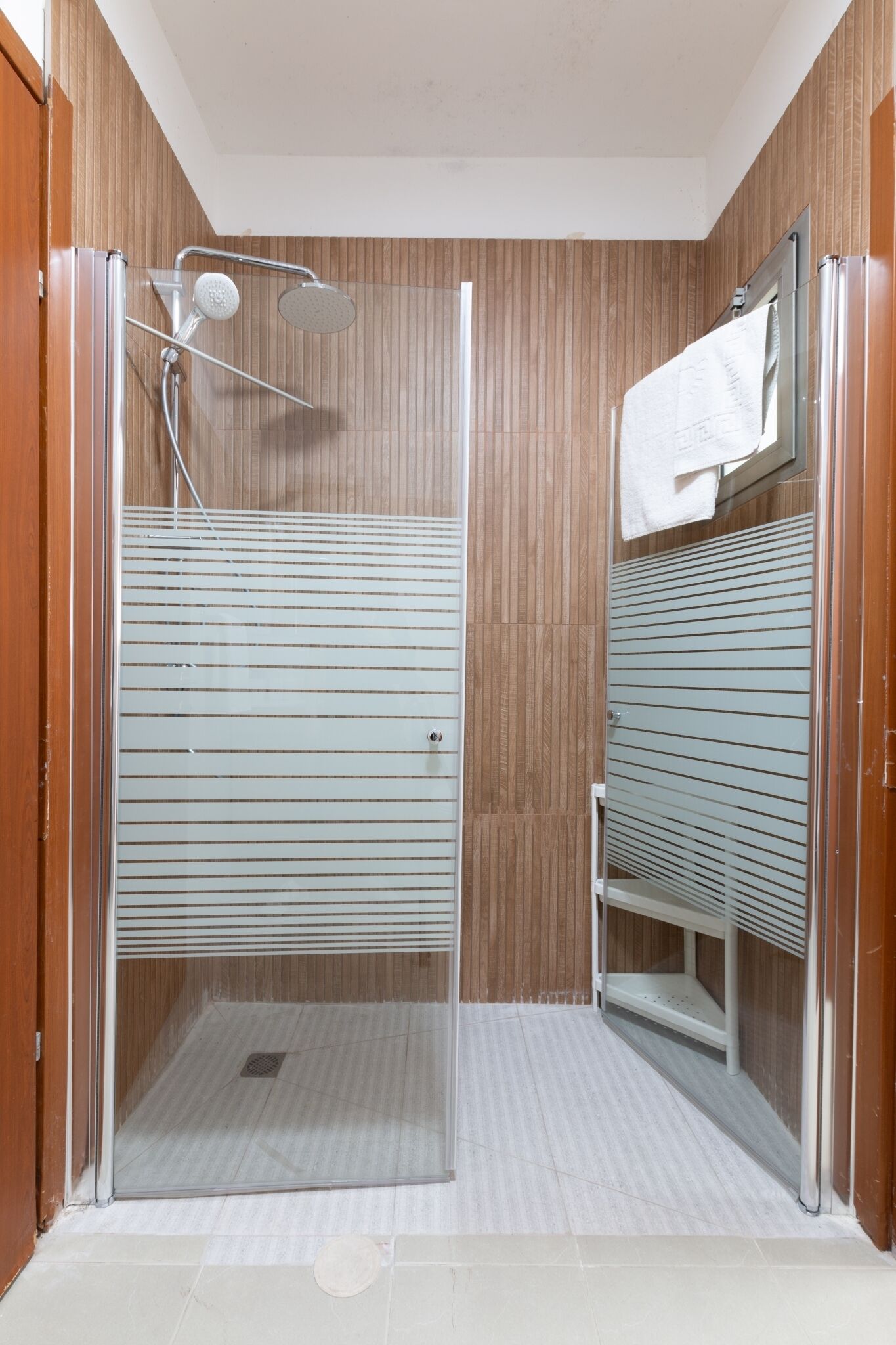 Una ducha a nivel con puerta de cristal, paneles de madera y suelo de baldosas.