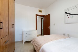 A bedroom with a bed, a wooden wardrobe, a white dresser, and a door leading to another room. - Stylish & Cozy Seaview Vacation APT (Bat Yam)