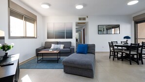 Ein modernes Wohnzimmer mit einem grauen Sofa, einem Couchtisch und einem Essbereich mit Tisch und Stühlen.