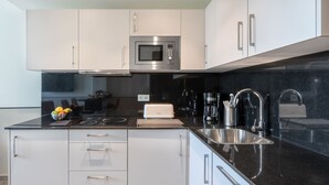 Une cuisine moderne avec des meubles blancs, un plan de travail noir, un four à micro-ondes encastré, un grille-pain et un évier.