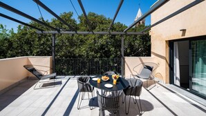 Une terrasse sur le toit, avec une table dressée pour deux personnes, entourée de chaises, et en arrière-plan, la vue sur le clocher d’une église.