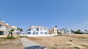 Un quartier résidentiel en bord de mer, avec des maisons modernes, un ciel dégagé et un chemin de gravier.
