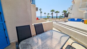 Un balcon avec une table et des chaises, donnant sur une plage bordée de palmiers et sur laquelle se trouve un poste de surveillance des sauveteurs.