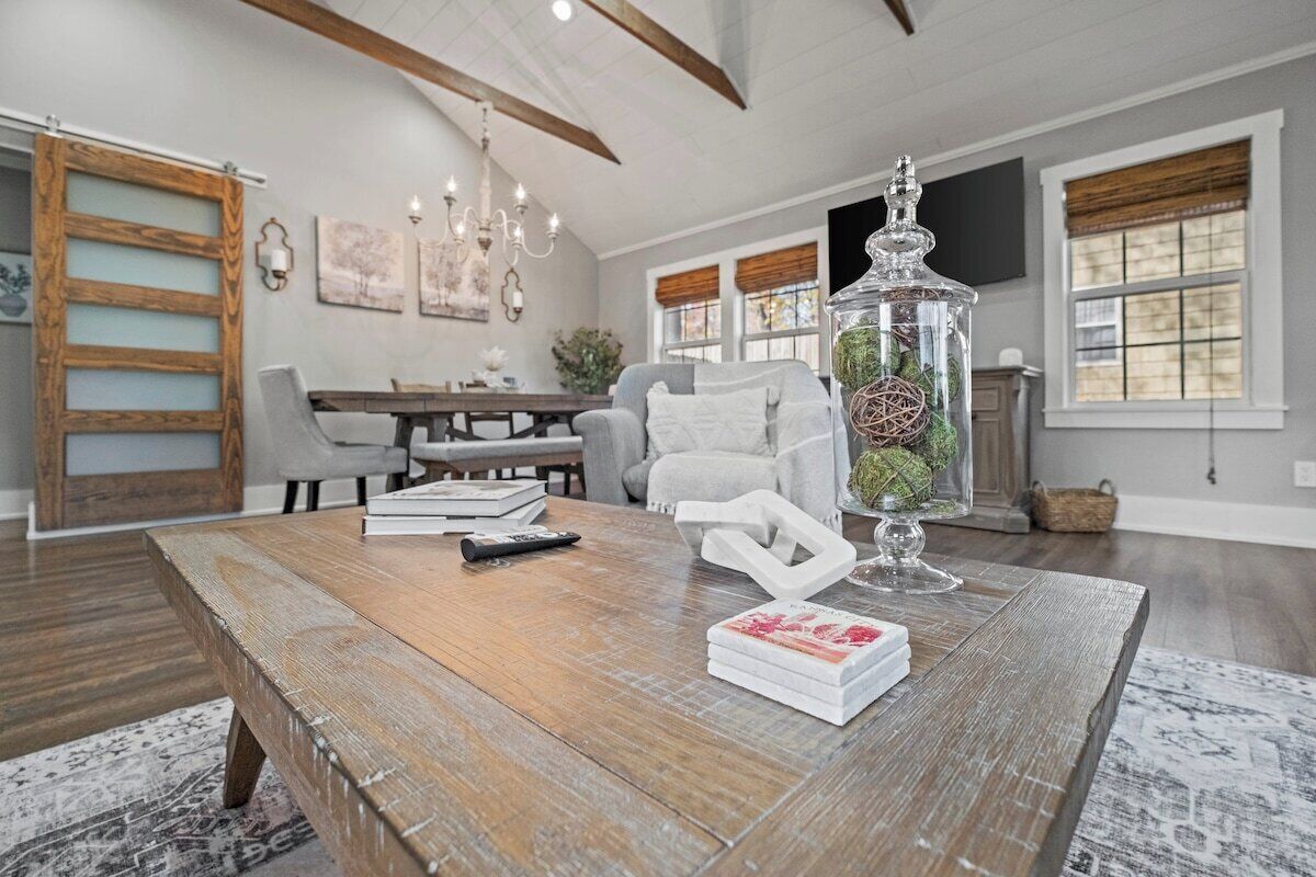 A spacious living room with a wooden coffee table, a glass vase with greenery, and a modern chandelier.