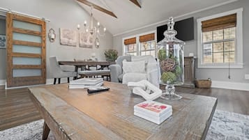 A spacious living room with a wooden coffee table, a glass vase with greenery, and a modern chandelier.