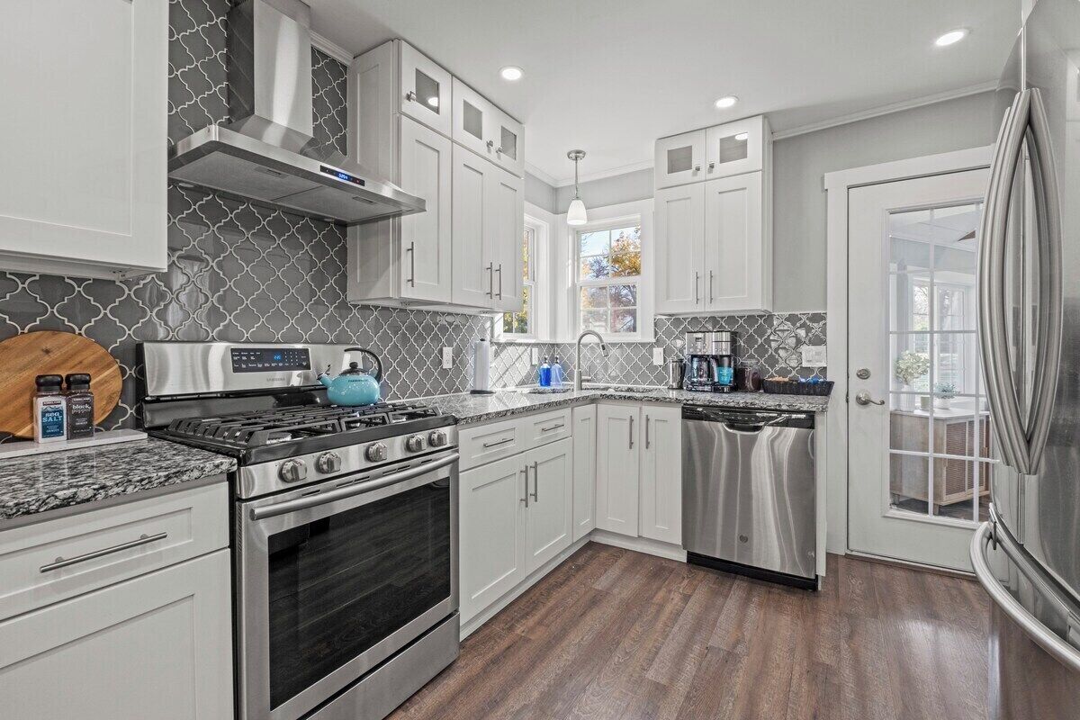 A modern kitchen with stainless steel appliances, white cabinetry, and a patterned backsplash.