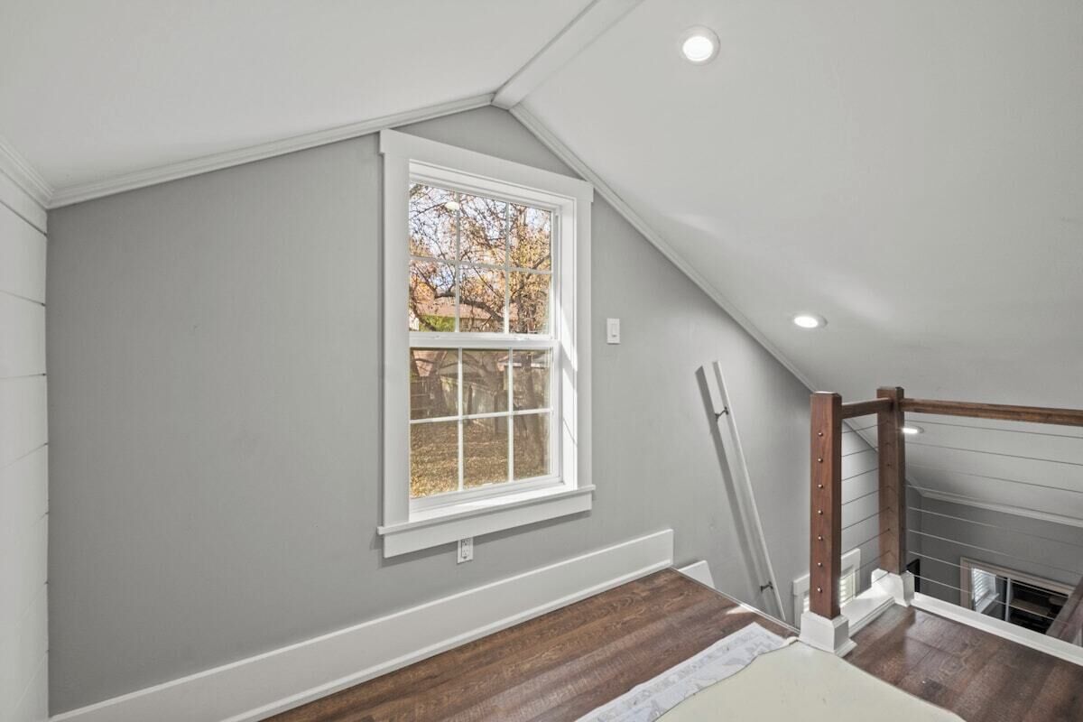 Una habitación con techo inclinado, ventana con vista a árboles y una escalera de madera.