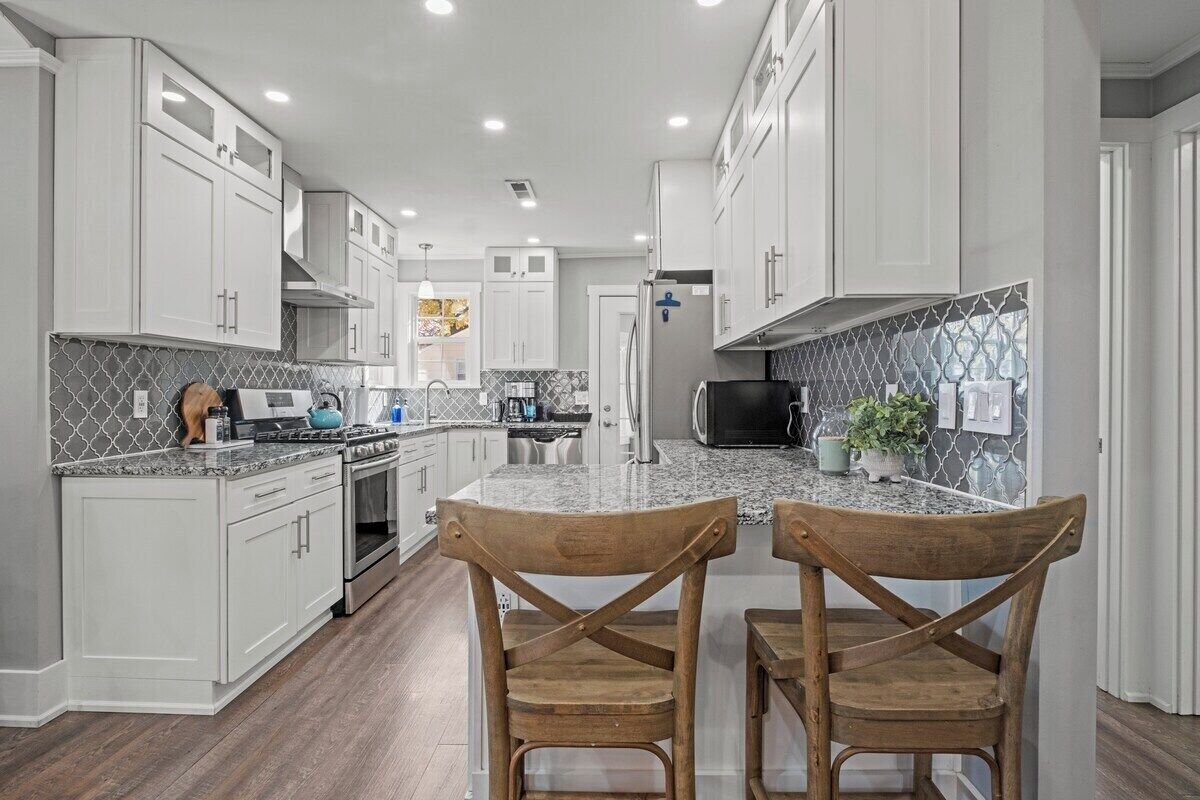 A modern kitchen with white cabinetry, granite countertops, and a central island with two wooden chairs.