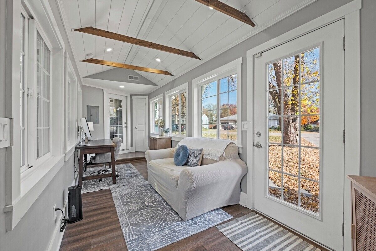 A room with a white sofa, a wooden table, and a large window with a view of trees.