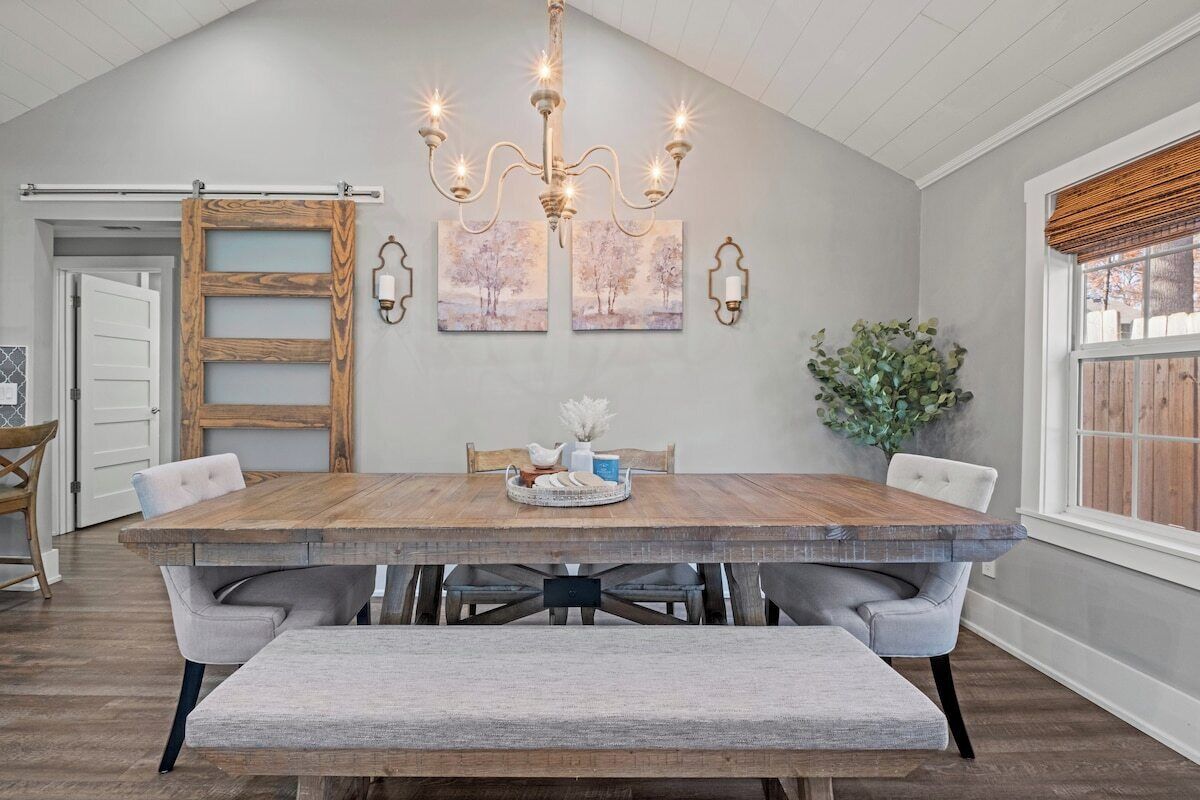 Comedor con mesa de madera, asientos tipo banco, lámpara de araña, obra de arte en la pared y una puerta corrediza de estilo rústico.