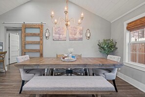 Comedor con mesa de madera, asientos tipo banco, lámpara de araña, obra de arte en la pared y una puerta corrediza de estilo rústico.