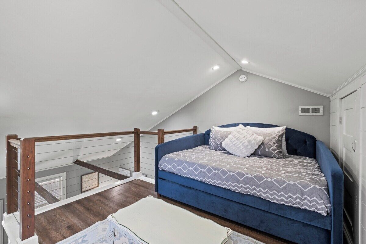 Un dormitorio con un sofá cama azul, un tapete blanco y una barandilla de madera.