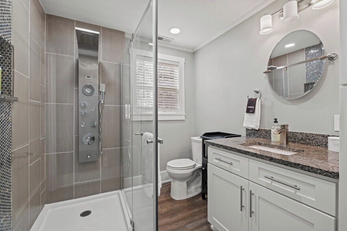 A modern bathroom with a glass-enclosed shower, a toilet, and a vanity with a mirror.
