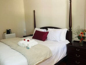 A neatly made bed with white linens, a beige throw blanket, and two red rose arrangements.