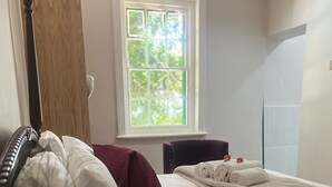 Quarto com uma cama, janela, cadeira e planta.