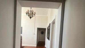 Um corredor com piso de madeira, paredes brancas e um candelabro.