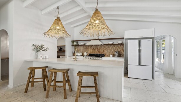 A modern kitchen with white cabinetry, a central island with stools, a built-in stove, and a refrigerator. - Sojourn at Sandy Beach - Pool, Beach, Slippery Dip, Style (Sandy Beach)