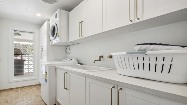 Een moderne wasruimte met een wasmachine, droger, spoelbak en een grote wasmand.