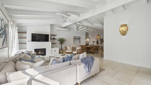 A spacious living room with a large sofa, a fireplace, a dining area, and a kitchen in the background. - Sojourn at Sandy Beach - Pool, Beach, Slippery Dip, Style (Sandy Beach)