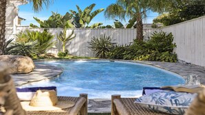 A swimming pool with a curved edge, surrounded by tropical plants and a white fence. - Sojourn at Sandy Beach - Pool, Beach, Slippery Dip, Style (Sandy Beach)