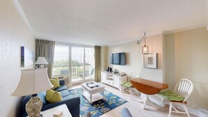 A modern living room with a sofa, coffee table, TV, and dining area. - Seaside Bliss Oceanfront1 Bdrm Ste at Bridgewater (Pawleys Island)