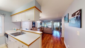 Eine moderne Küche mit weißen Schränken und einer Holz Arbeitsplatte, ein Essbereich mit Tisch und Stühlen sowie ein Wohnzimmer mit einer Couch und einem großen Fenster.