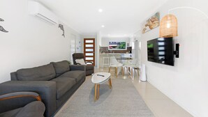 A modern living room with a grey sofa, a small white table, and a TV mounted on the wall.