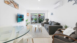 A modern living room with a glass dining table, grey sofa, and a TV mounted on the wall.