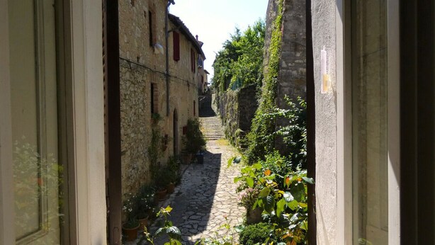Une ruelle étroite, pavée de pierres, bordée d’immeubles dont les fenêtres et les portes sont bien visibles.