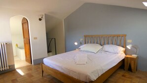 Une chambre à coucher avec un lit en bois, du linge de lit blanc, une table de chevet avec une lampe et un radiateur.
