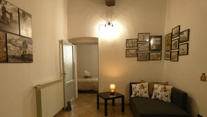 A cozy living room with a dark sofa, a small table with a lamp, and a hallway leading to a bedroom. - Scappo in Umbria, CasaLina (Amelia)