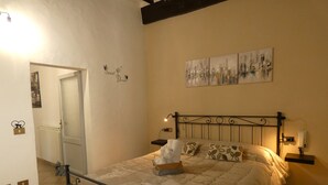 A bedroom with a bed, a nightstand, a wall-mounted shelf, and a door leading to another room. - Scappo in Umbria, CasaLina (Amelia)