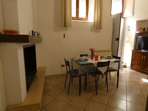 Ein Essbereich mit einem Tisch für vier Personen, Stühlen, einer Blumenvase und einem Fernseher in der Ecke.