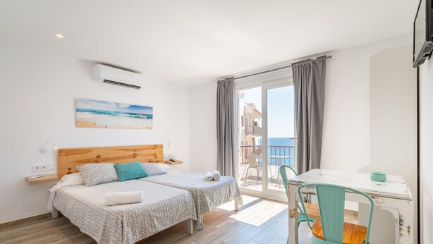 A bedroom with two beds, a balcony, and a dining area. - Apartamentos Marivent (Felanitx)