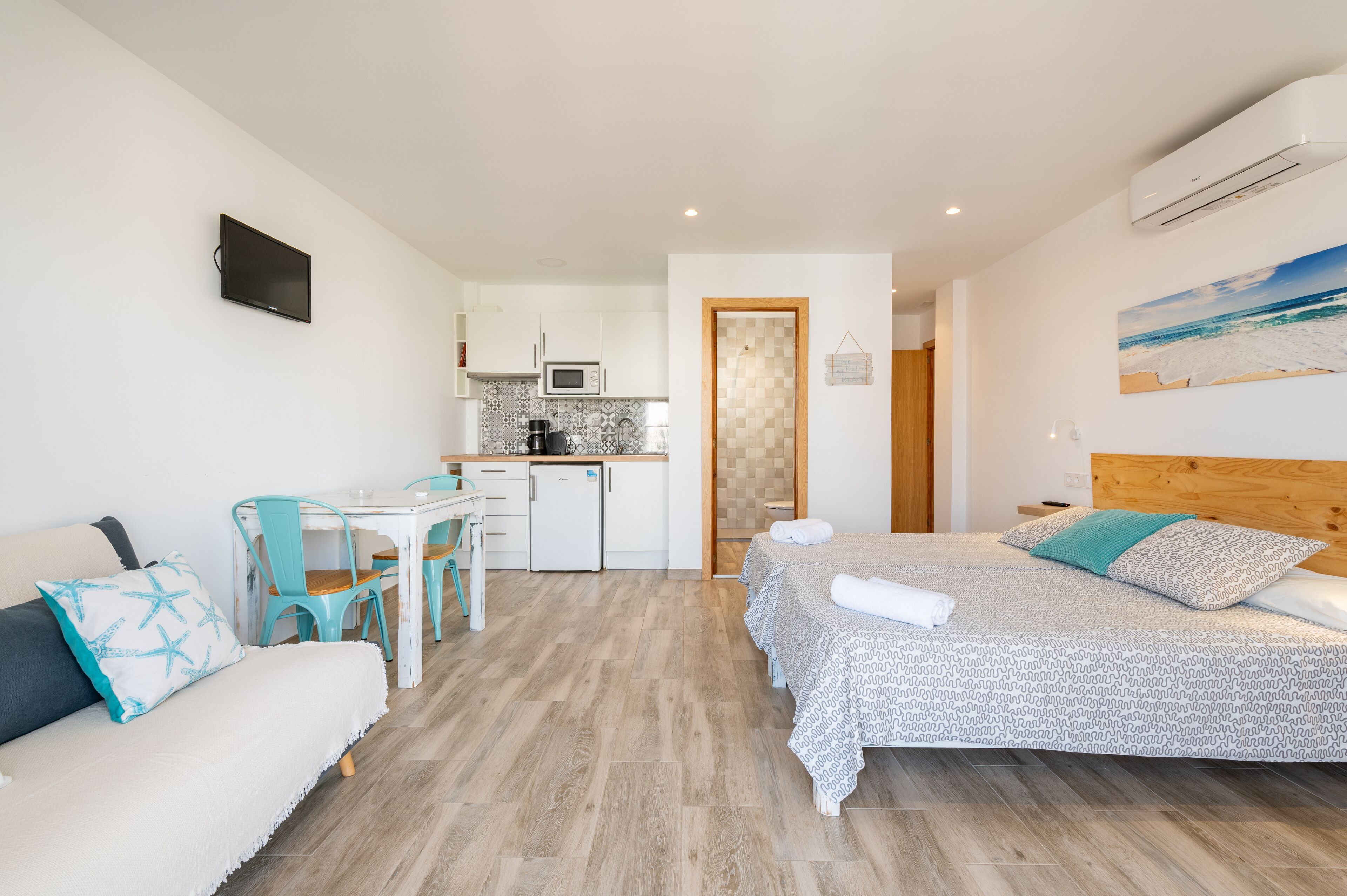 Habitación de hotel pequeña con cama, una kitchenette, un área de comedor y un baño visible a través de una puerta abierta.