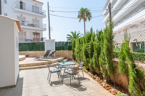A patio with a table and chairs, surrounded by greenery and a fence. - Apartamentos Marivent (Felanitx)
