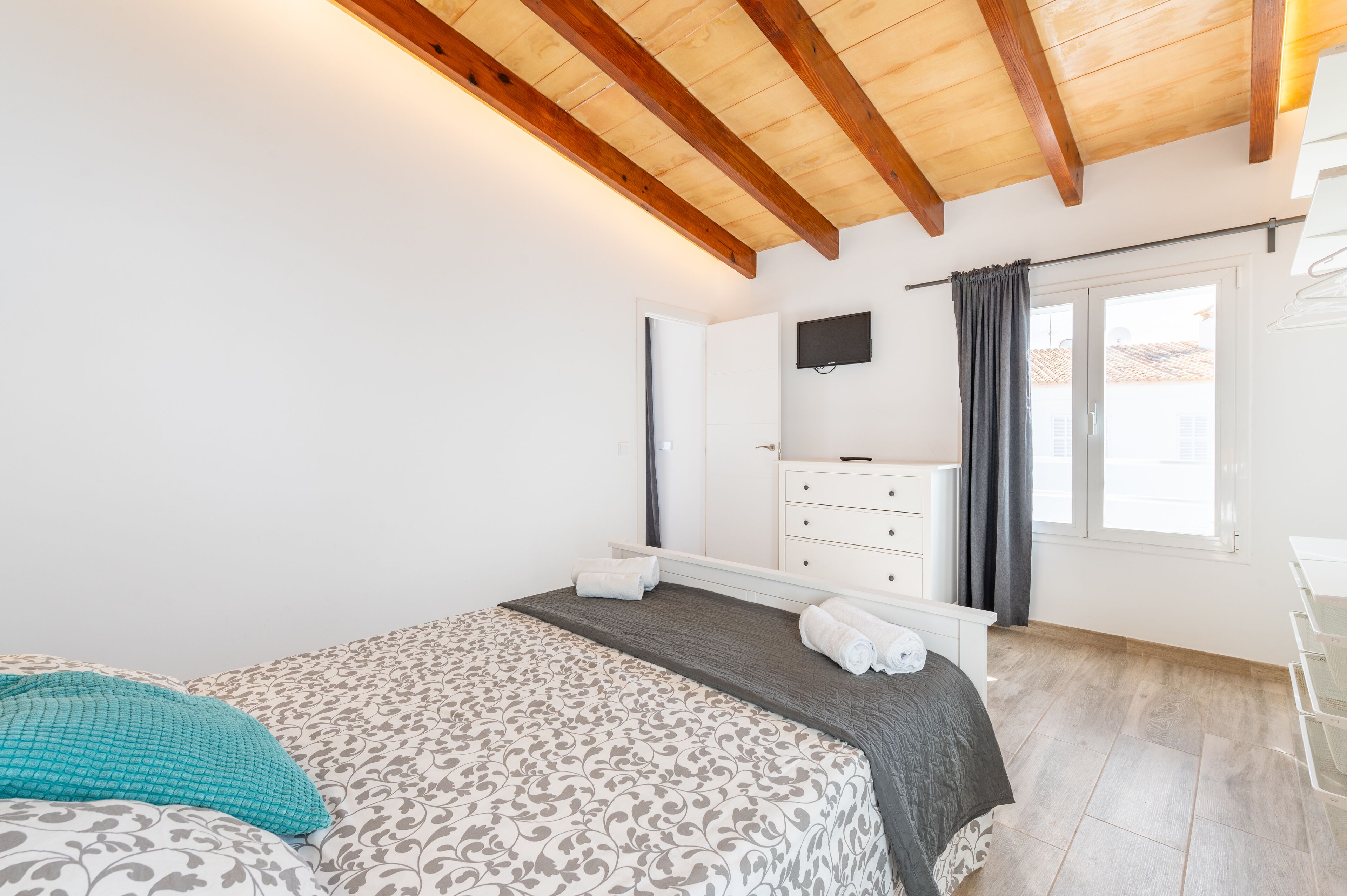 Un dormitorio con cama, cómoda, televisor y ventana con cortinas.