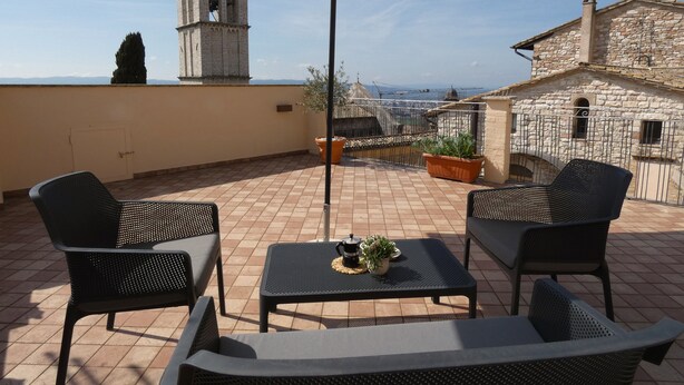 A terrace with outdoor furniture, a large umbrella, and a view of a historic building with a bell tower. - SCAPPO IN UMBRIA, la casa di Eude (Assisi)