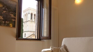 A room with a white sofa, a window with a view of a historic building, and a radiator on the wall. - SCAPPO IN UMBRIA, la casa di Eude (Assisi)