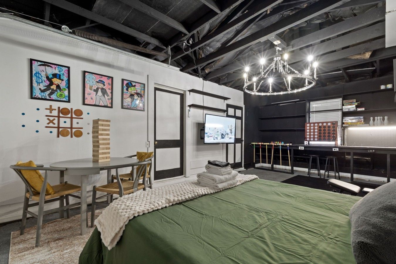 A room with a bed, a table with chairs, a television, and artwork on the walls.