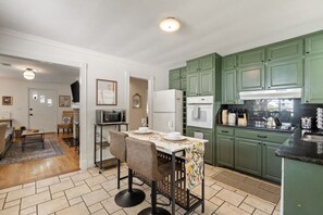 Cozinha compacta com armários verdes, área de refeições com duas cadeiras, micro-ondas e geladeira.