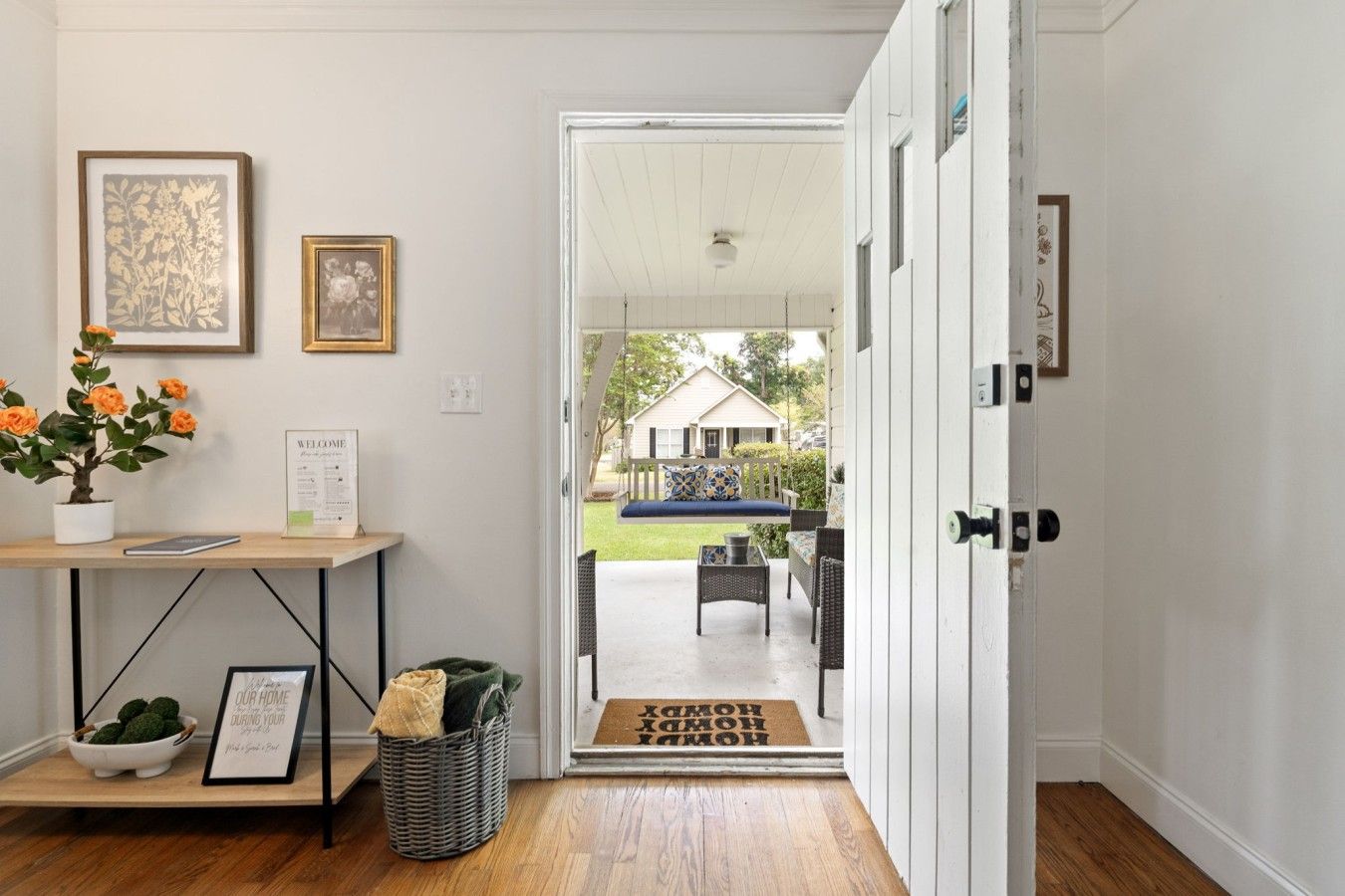 A clean, well-lit entryway with a wooden floor, a welcome sign, a framed picture, and a potted plant.