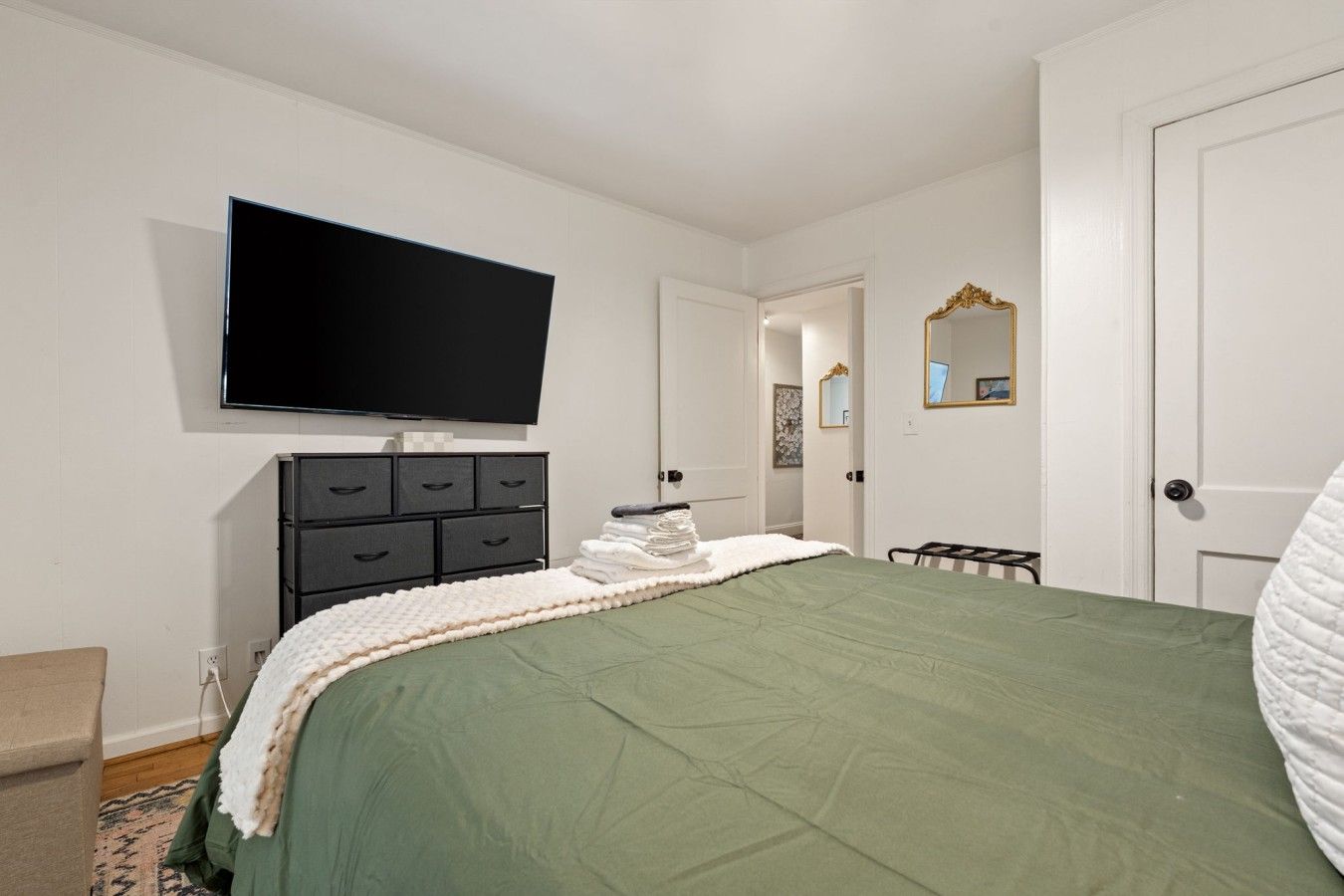 Een slaapkamer met een bed, een dressoir, een televisie en een deur.